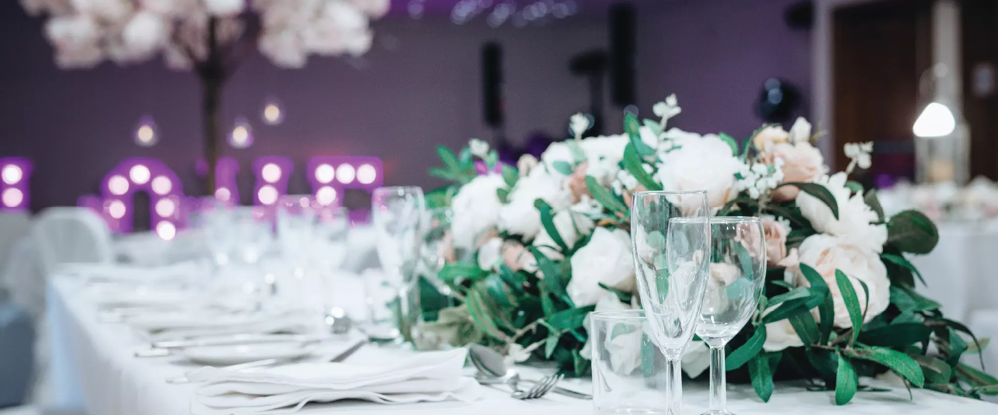 A wedding table beautifully set with flowers. The word LOVE appears in the background in large, lit up purple letters.